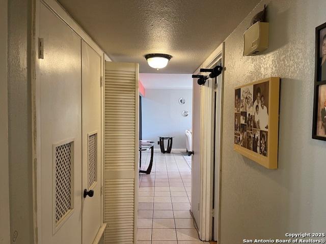 hallway with light tile patterned floors, a textured ceiling, and a textured wall