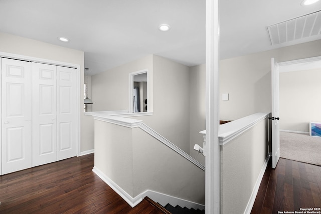 hallway featuring dark wood-style floors, baseboards, visible vents, and an upstairs landing