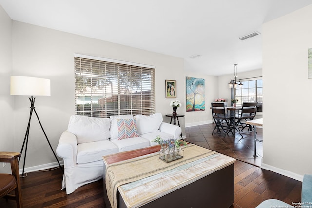 living area featuring dark wood-type flooring, a chandelier, visible vents, and baseboards