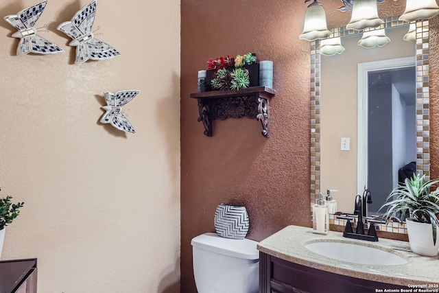 half bathroom with a textured wall, vanity, and toilet