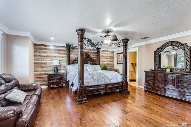 bedroom featuring a textured ceiling, hardwood / wood-style flooring, visible vents, baseboards, and ornamental molding