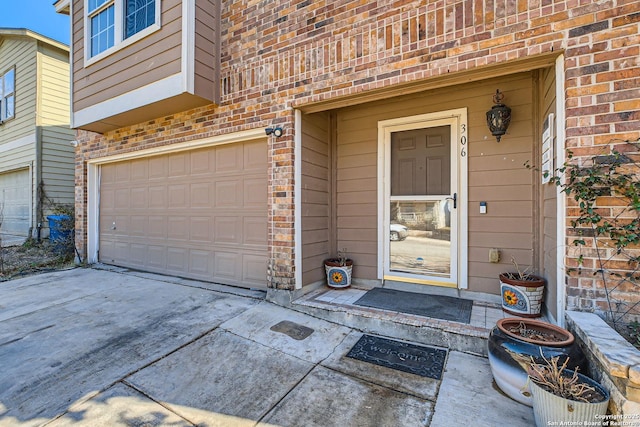 doorway to property with driveway, a garage, and brick siding