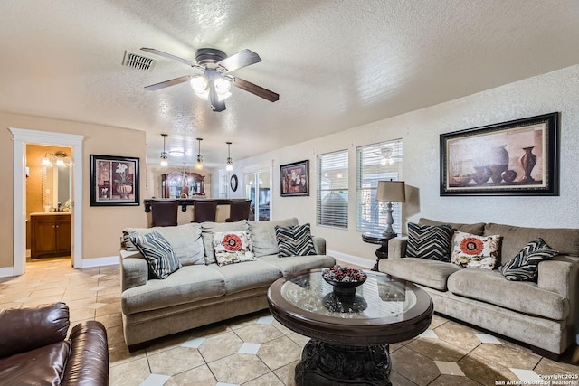 living area with a textured ceiling, ceiling fan, light tile patterned floors, visible vents, and baseboards