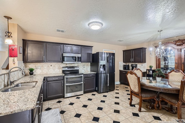 kitchen with a chandelier, light stone counters, stainless steel appliances, a sink, and visible vents