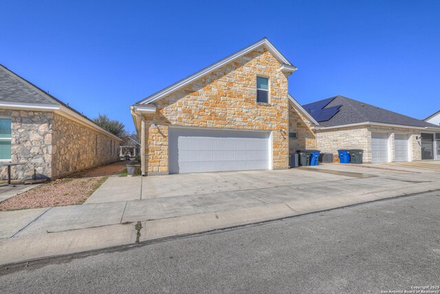 948 Hudson, New Braunfels, TX 78130 - view of front facade featuring a garage, roof mounted solar panels, stone siding, and concrete driveway