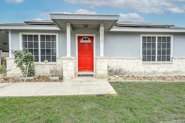 doorway to property with stone siding, stucco siding, a yard, and solar panels