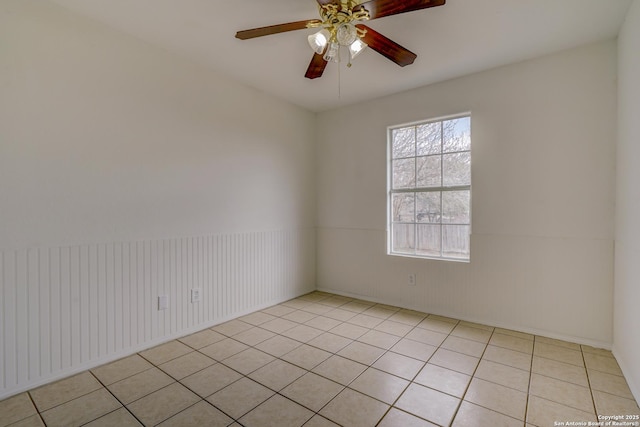 spare room featuring light tile patterned floors, ceiling fan, and wainscoting