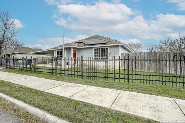 view of front of house with solar panels, a fenced front yard, a front yard, and stucco siding