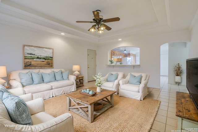 living area featuring arched walkways, light tile patterned floors, a raised ceiling, and a ceiling fan