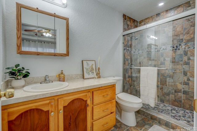 bathroom featuring a textured wall, toilet, vanity, a shower stall, and stone finish flooring