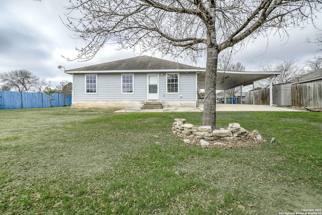 rear view of house with a carport, a lawn, driveway, and fence