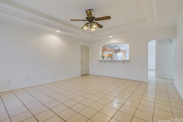 unfurnished room featuring arched walkways, ceiling fan, light tile patterned flooring, and a raised ceiling