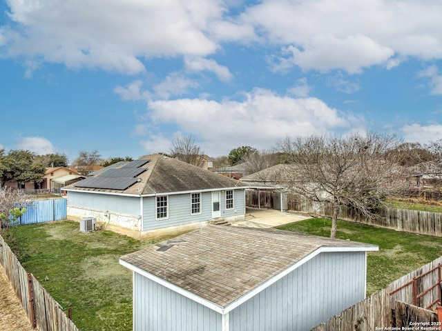 back of property with central AC, a yard, solar panels, and a fenced backyard