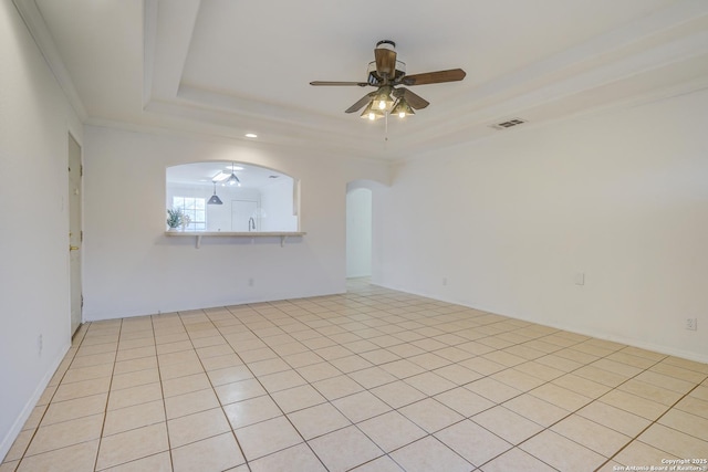 empty room with visible vents, arched walkways, a ceiling fan, ornamental molding, and a tray ceiling