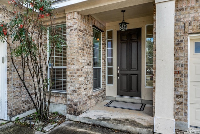 view of exterior entry with a garage, brick siding, and a porch