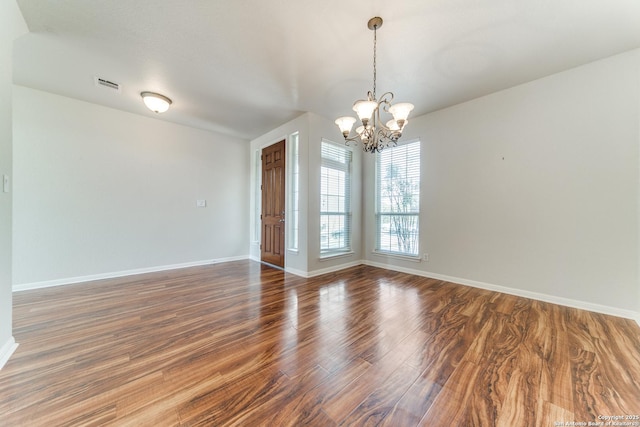 empty room featuring baseboards, visible vents, a chandelier, and wood finished floors