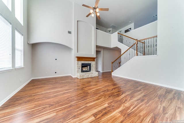 unfurnished living room featuring a towering ceiling, stairs, wood finished floors, and a stone fireplace