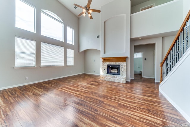 unfurnished living room featuring a stone fireplace, stairway, baseboards, and wood finished floors