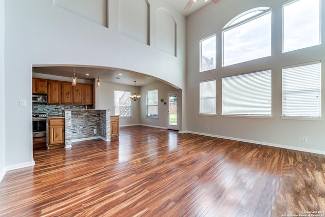 unfurnished living room with dark wood-style floors, arched walkways, a towering ceiling, and baseboards