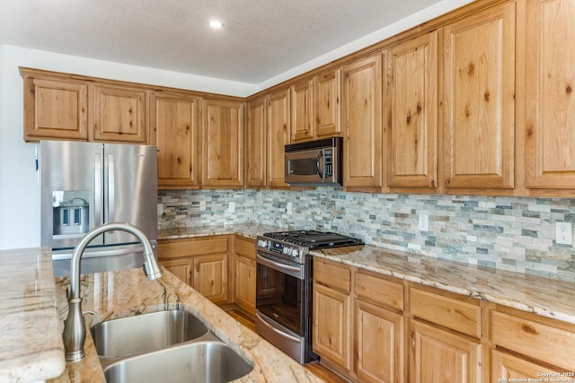 kitchen featuring decorative backsplash, appliances with stainless steel finishes, light stone counters, a textured ceiling, and a sink