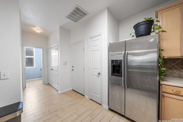 kitchen featuring visible vents, baseboards, light wood-style floors, stainless steel fridge with ice dispenser, and decorative backsplash