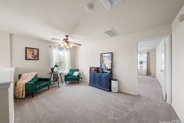 living area with light colored carpet, visible vents, a ceiling fan, a textured ceiling, and baseboards