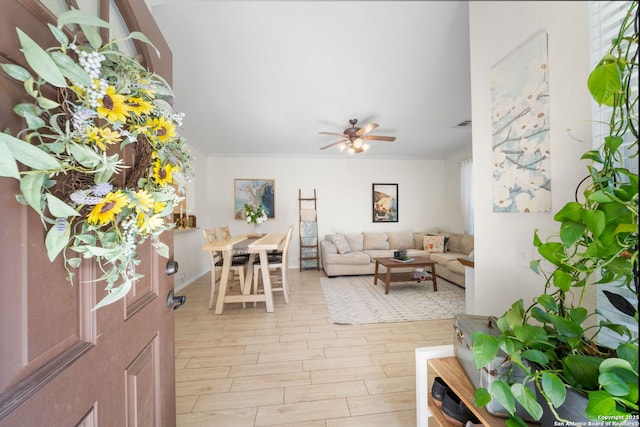 living area with ceiling fan, ornamental molding, and wood finish floors