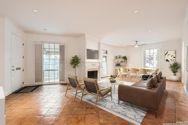 living area featuring recessed lighting, a fireplace with flush hearth, ornamental molding, a ceiling fan, and baseboards