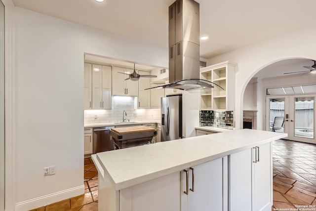 kitchen with island range hood, decorative backsplash, ceiling fan, stainless steel appliances, and open shelves