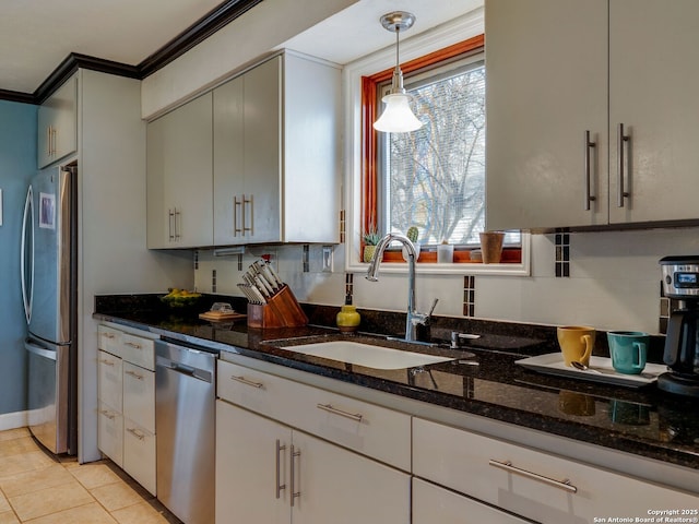 kitchen featuring appliances with stainless steel finishes, dark stone countertops, crown molding, pendant lighting, and a sink