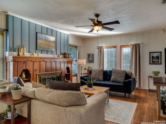 living area featuring ceiling fan, a glass covered fireplace, plenty of natural light, and wood finished floors