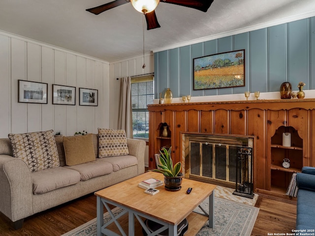 living room with crown molding, ceiling fan, wood finished floors, and a glass covered fireplace