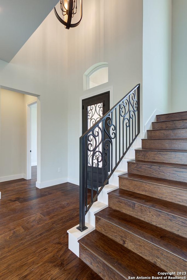 stairs with an inviting chandelier, a high ceiling, baseboards, and wood finished floors