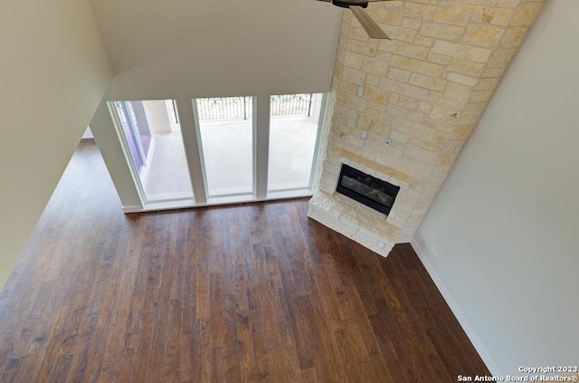 unfurnished living room with baseboards, dark wood-style flooring, and a stone fireplace