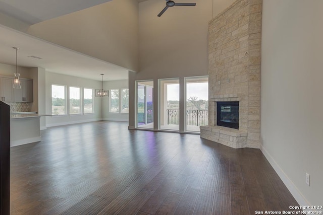 unfurnished living room featuring a ceiling fan, dark wood-style flooring, a stone fireplace, and baseboards