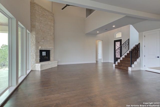 unfurnished living room featuring a high ceiling, baseboards, dark wood-style flooring, and a stone fireplace