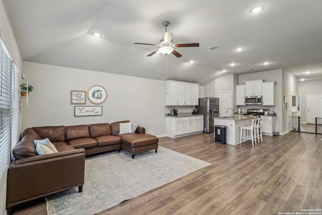 living area with dark wood-style flooring, visible vents, vaulted ceiling, and ceiling fan