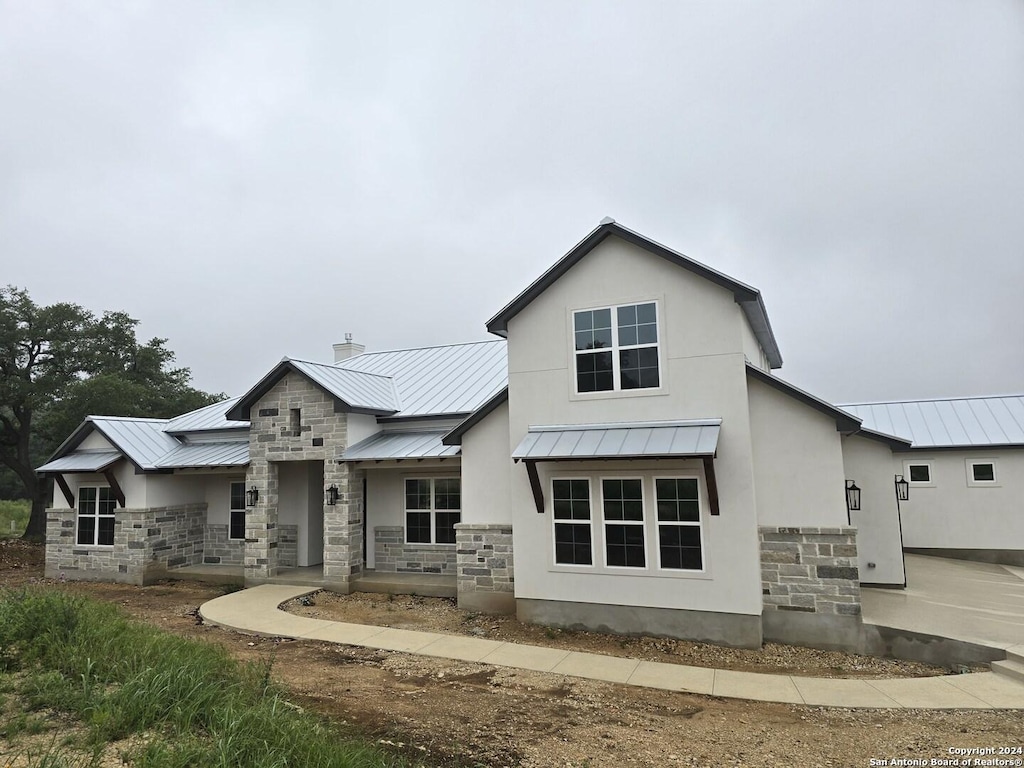 back of property with a standing seam roof, stone siding, a chimney, and metal roof