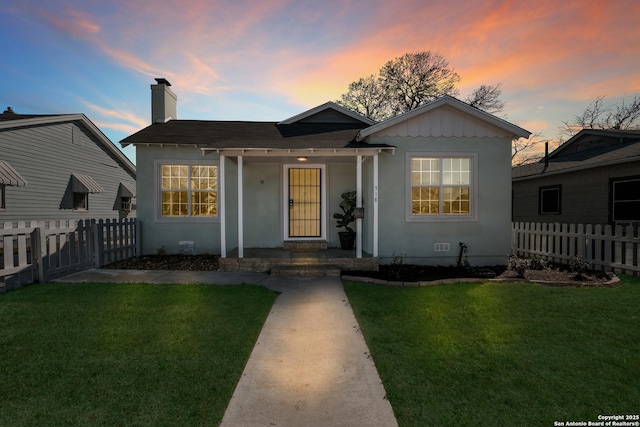 bungalow-style home with a yard, fence, and a chimney