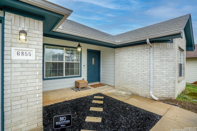 entrance to property with a shingled roof, a porch, and brick siding