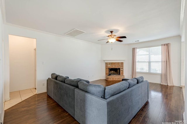 living area with a brick fireplace, visible vents, ceiling fan, and wood finished floors