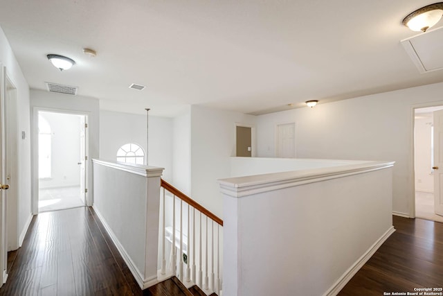 corridor with attic access, visible vents, dark wood-style flooring, and an upstairs landing