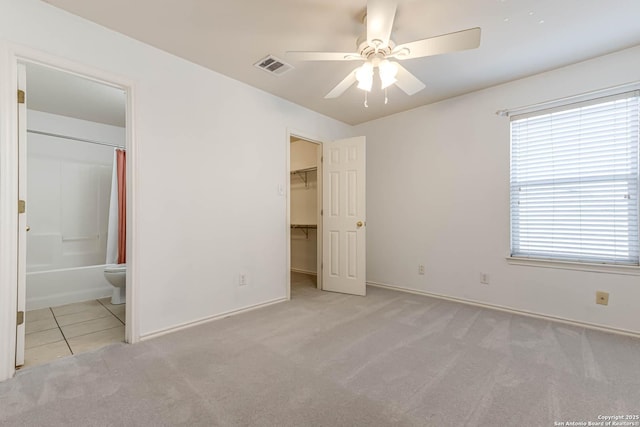 unfurnished bedroom featuring carpet, a walk in closet, visible vents, ensuite bathroom, and tile patterned floors