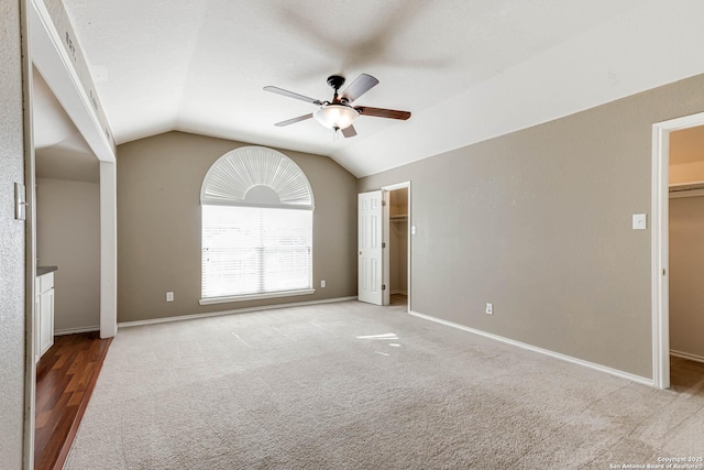 unfurnished bedroom featuring vaulted ceiling, carpet floors, a walk in closet, and baseboards