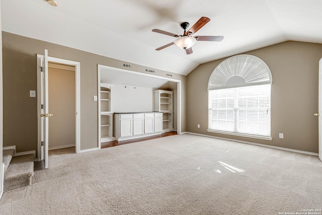 spare room with baseboards, ceiling fan, vaulted ceiling, carpet flooring, and built in shelves