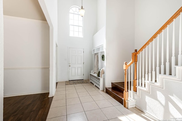 foyer entrance with stairway, light tile patterned flooring, a towering ceiling, and baseboards