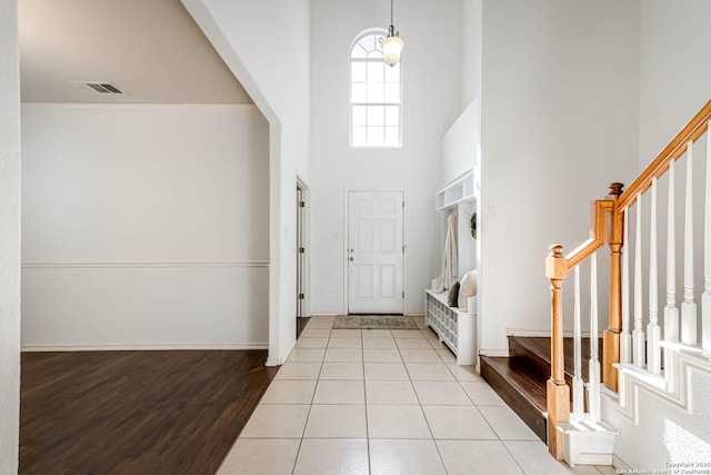 foyer entrance featuring light tile patterned floors, visible vents, stairway, a high ceiling, and baseboards