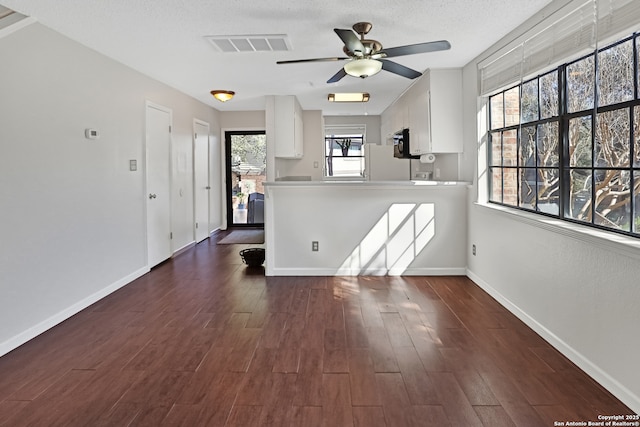 empty room featuring baseboards, visible vents, a ceiling fan, dark wood-type flooring, and a textured ceiling