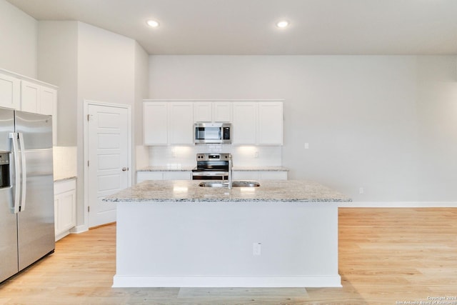 kitchen featuring an island with sink, light stone countertops, stainless steel appliances, light wood-style floors, and backsplash