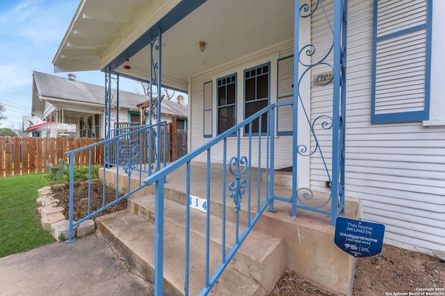 view of exterior entry with covered porch and fence